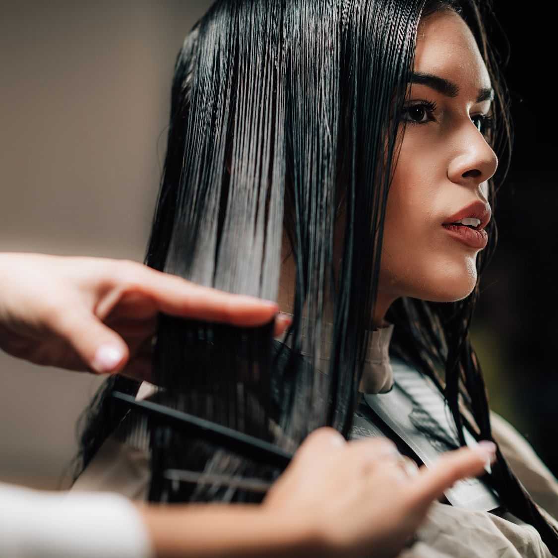 Stylist cutting a woman's long hair at a salon.