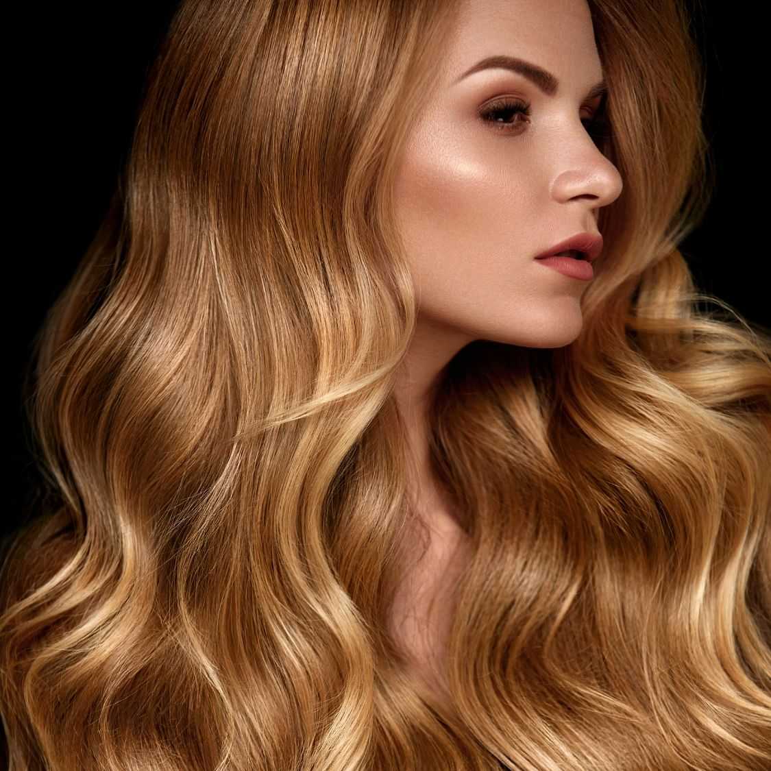 Woman with voluminous blonde wavy hair on dark background.