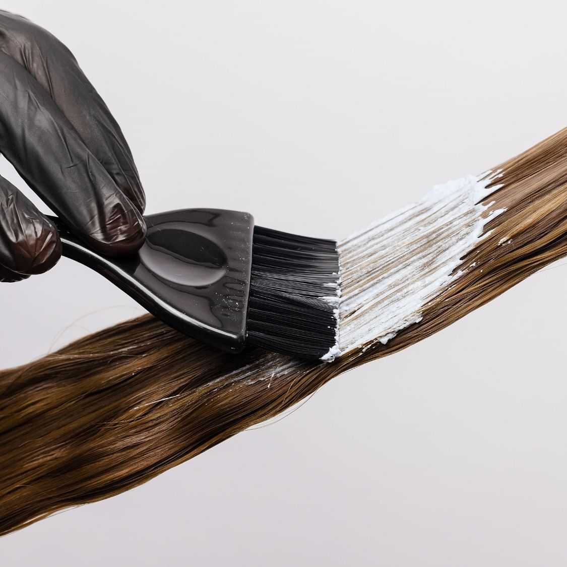 Applying hair dye to a strand of hair with a brush.