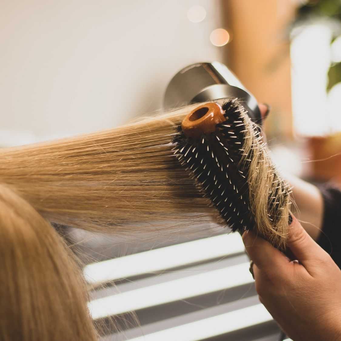 Person getting their blonde hair brushed and styled with a round brush.