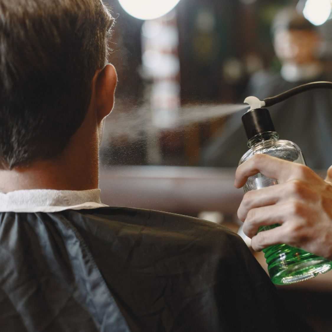 A barber sprays water onto a client's hair before cutting.