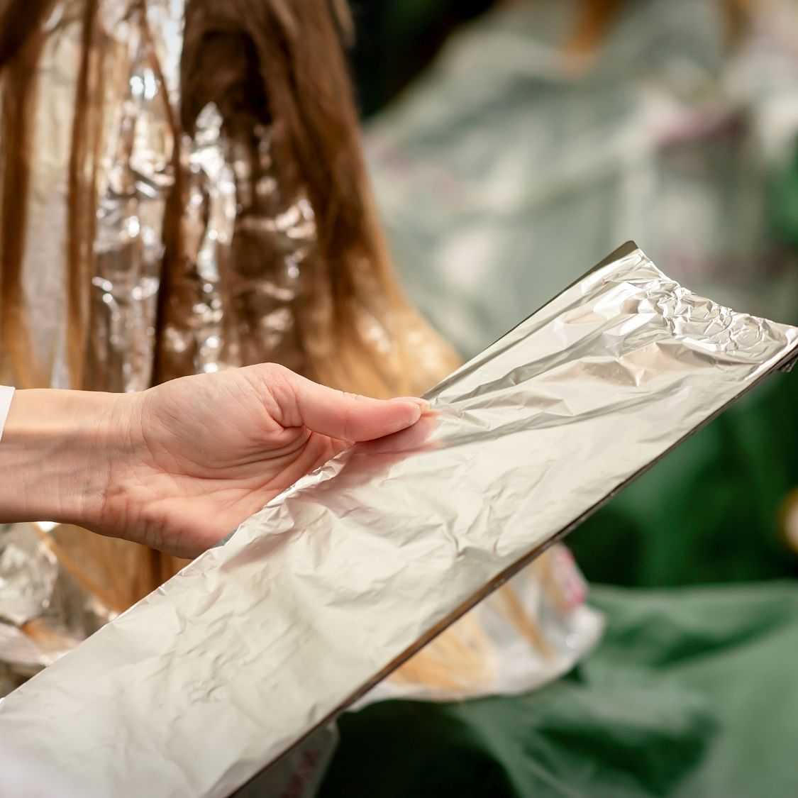 Hand holding a sheet of aluminum foil with a blurred background.