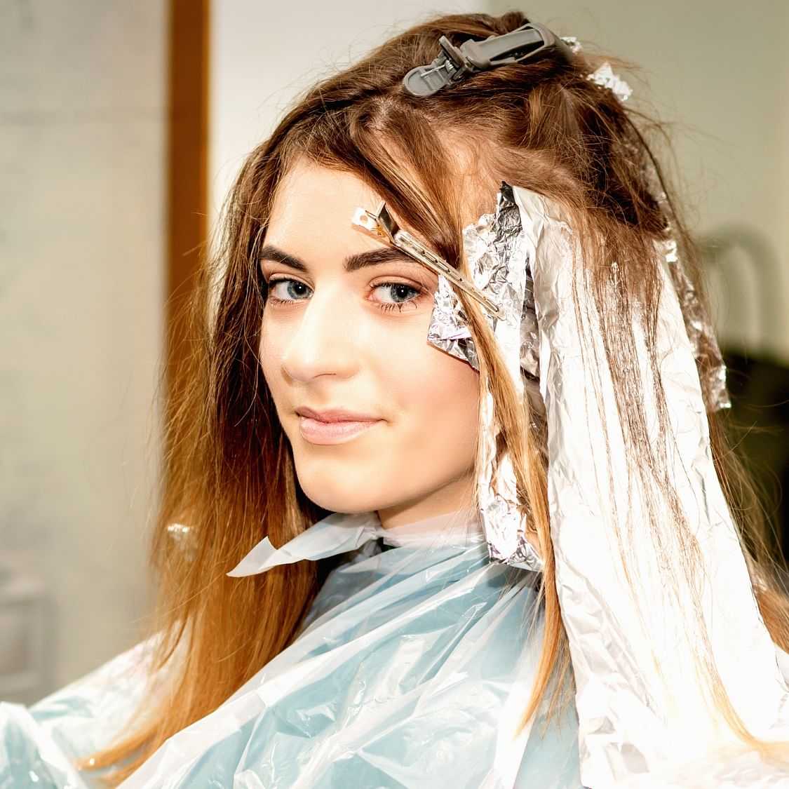 Woman smiling with hair in foils during a highlighting treatment.