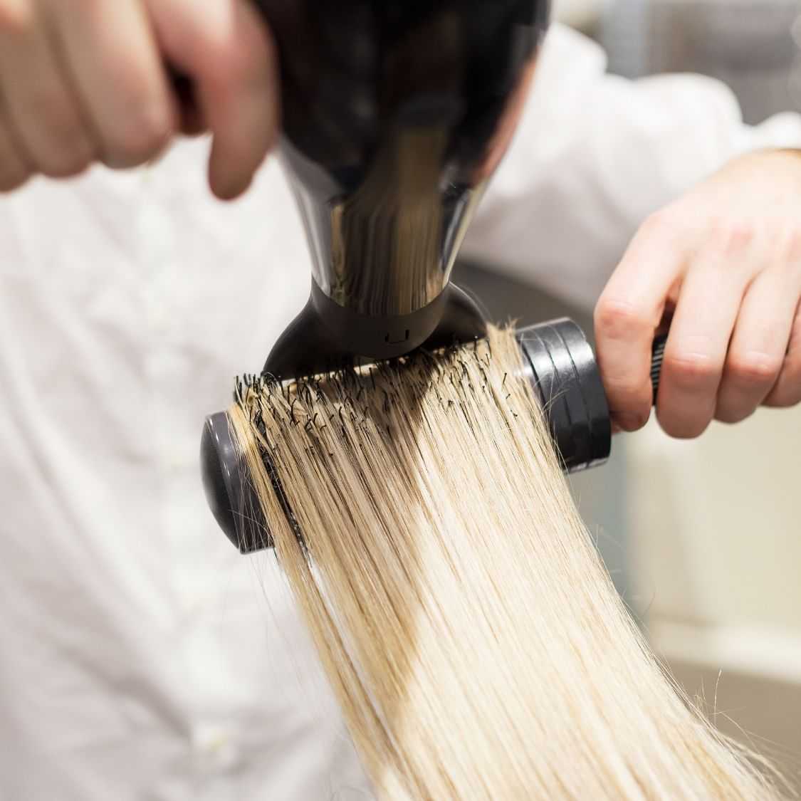 Hairdresser trimming ends of long blonde hair with electric clippers.