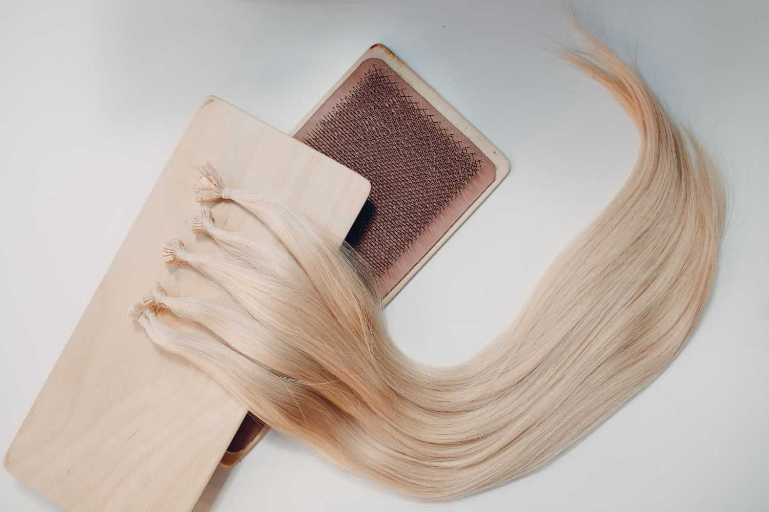 Blonde hair extensions next to a brush on a white background.