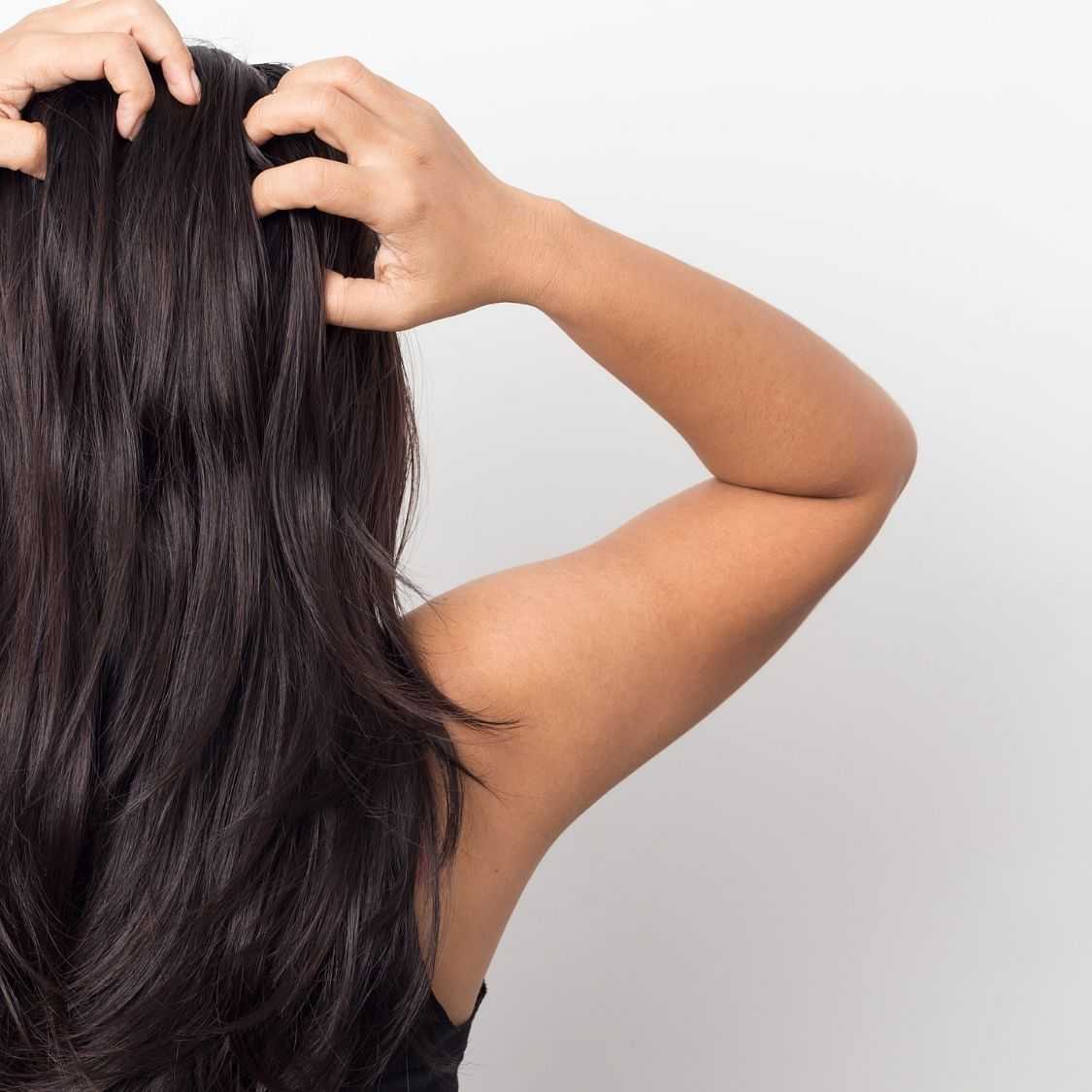 Person scratching head, showing long, dark hair, isolated on light background.