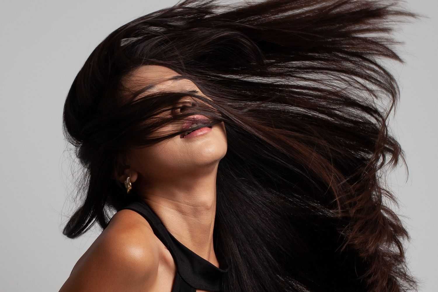 Woman with hair flipping covering her face against a gray backdrop.