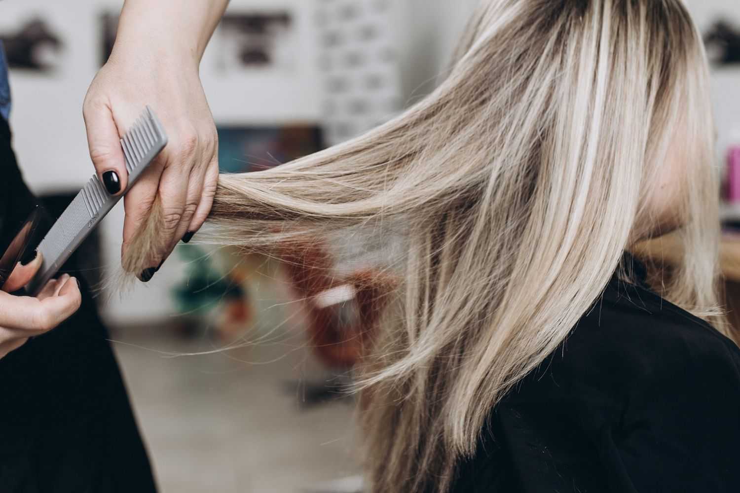 Person getting their blonde hair combed in a salon.