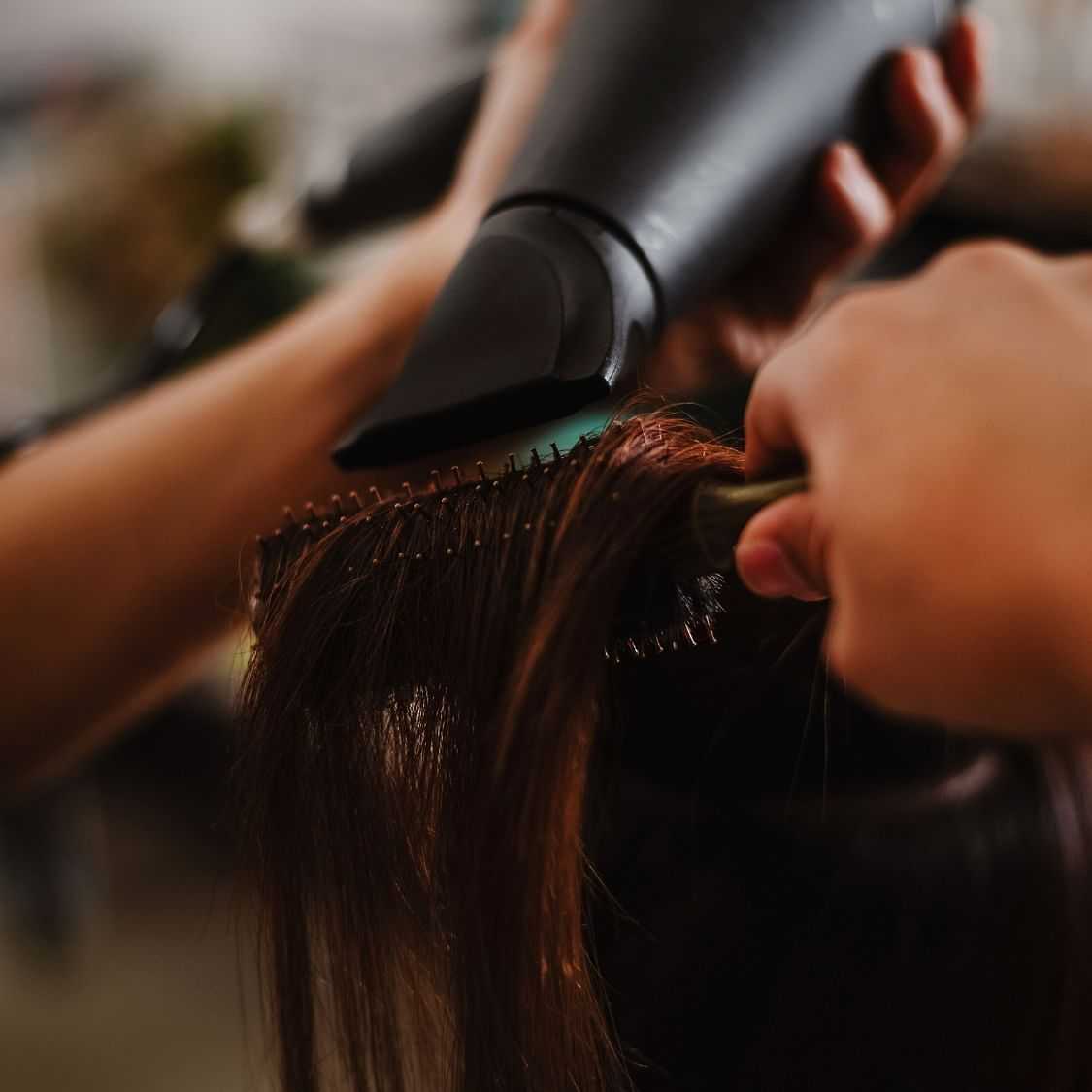 Hairdresser blow-drying a client's hair at a salon.